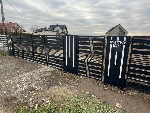 Geometryczna brama stalowa z furtką — szeroki widok od strony ulicy