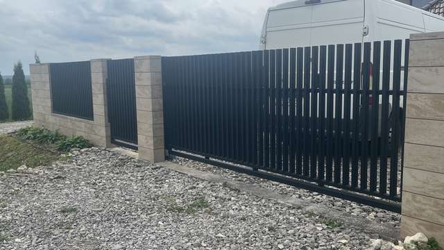 Czarna brama palisadowa z pionowymi profilami przy nowoczesnym domu