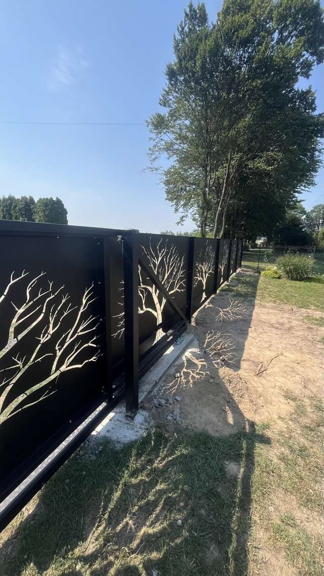 Czarne ogrodzenie dekoracyjne CNC na tle zieleni przydomowego ogrodu