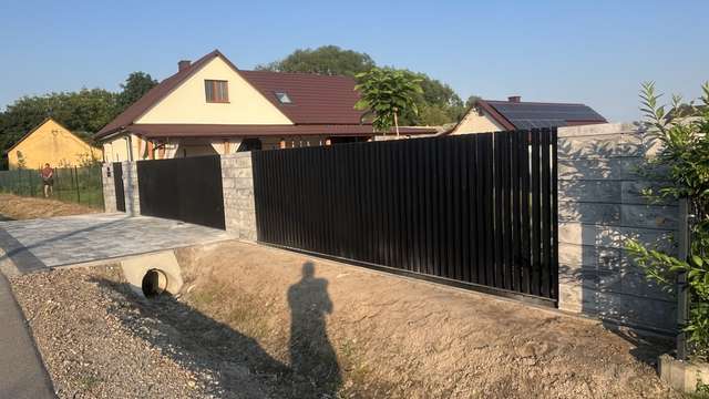 Narożnik czarnego ogrodzenia grzebieniowego przy podjeździe z kostki
